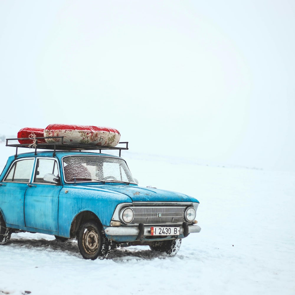 Blue sedan parked on a snowy road in crisp daylight, shown in a tight exterior close-up