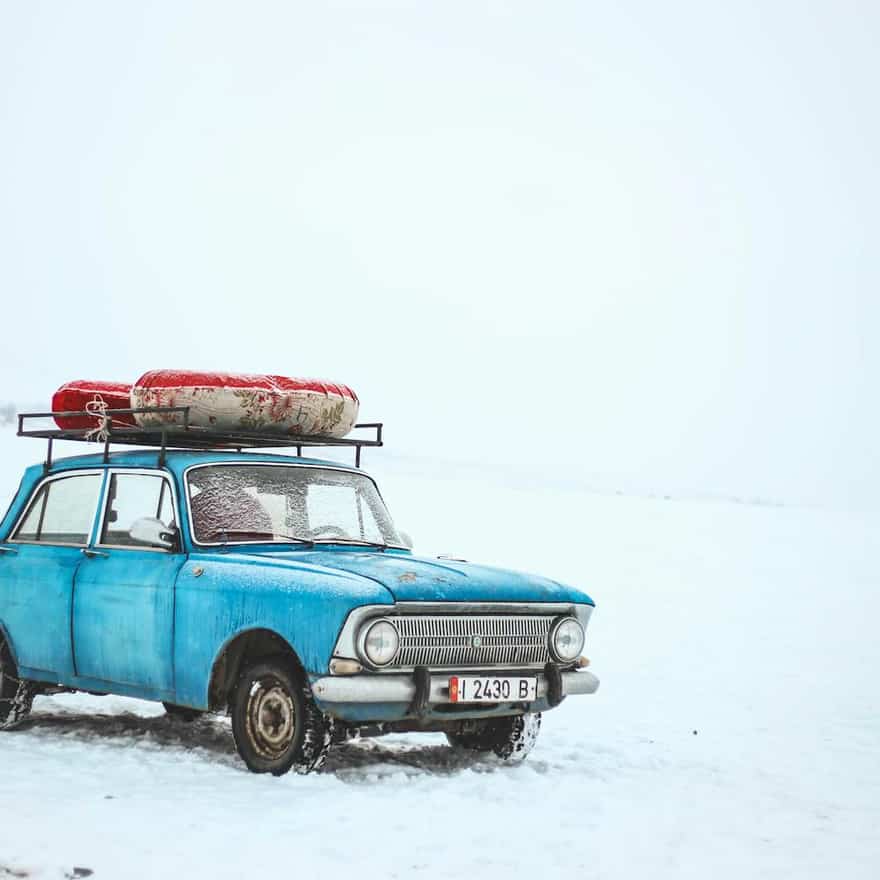 Blue sedan on a snowy road in daylight, shown in a tight exterior close-up