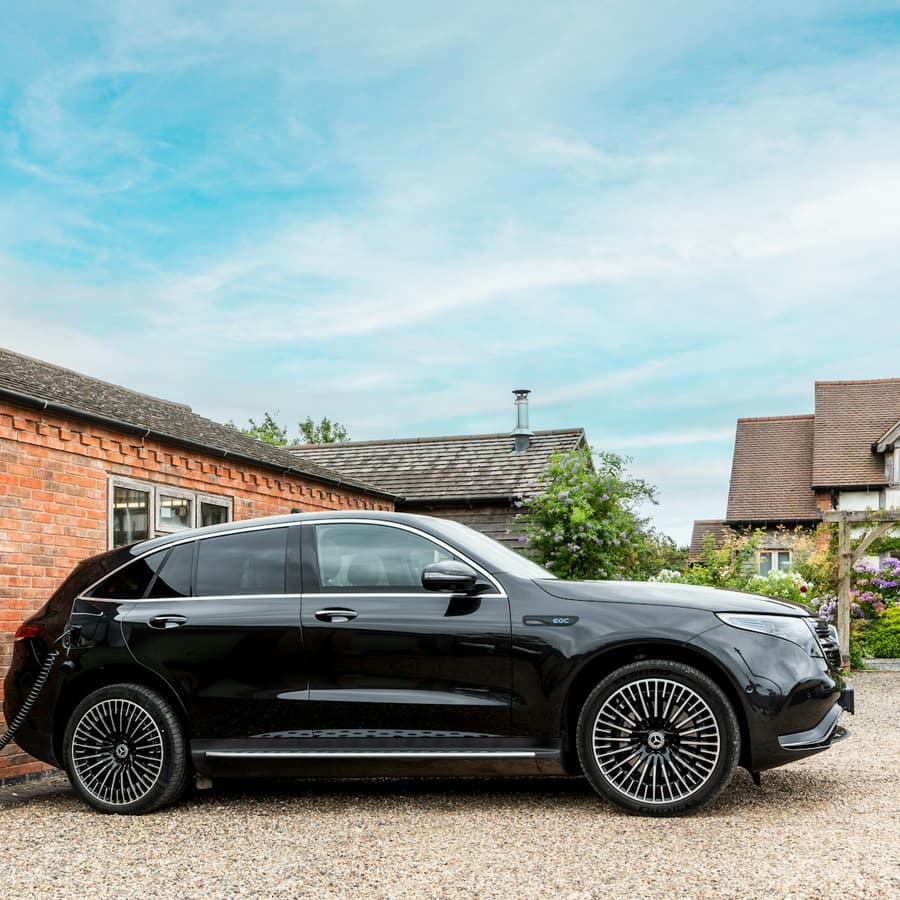 Black electric car charging at a wall unit beside a brick building in a close exterior view